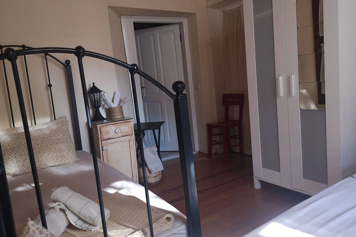 A bedroom with a four-poster bed, a wooden dresser, a chair, and a wardrobe.