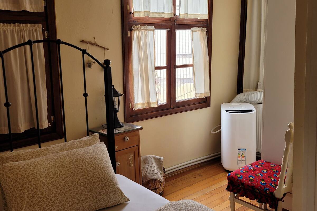 A bedroom with a bed, a bedside table, a chair, a window with curtains, and a radiator.