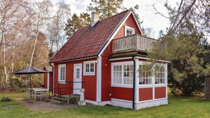 A red wooden house with a balcony, a covered patio with chairs, and a window overlooking the yard. - 2 bedroom gorgeous home in Höllviken (Höllviken)