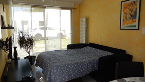 A bedroom with a bed, a desk, a chair, a potted plant, and a window with a view of a parked car outside. - Holiday house near sea and shops (La Baule)