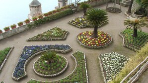 Un jardín con parterres florales geométricos y una pequeña torre.