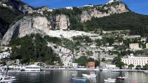 Un pueblo costero con un puerto deportivo, edificios en una ladera y un acantilado destacado.