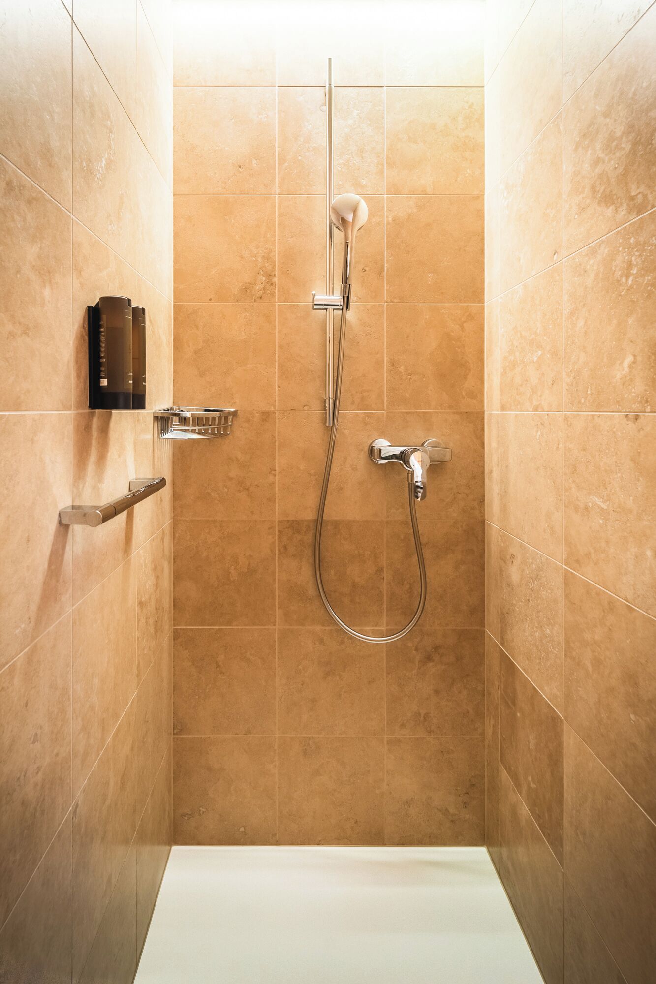 Un espace douche moderne doté d’un pommeau de douche à main, d’un robinet mural et d’un panneau de commande.