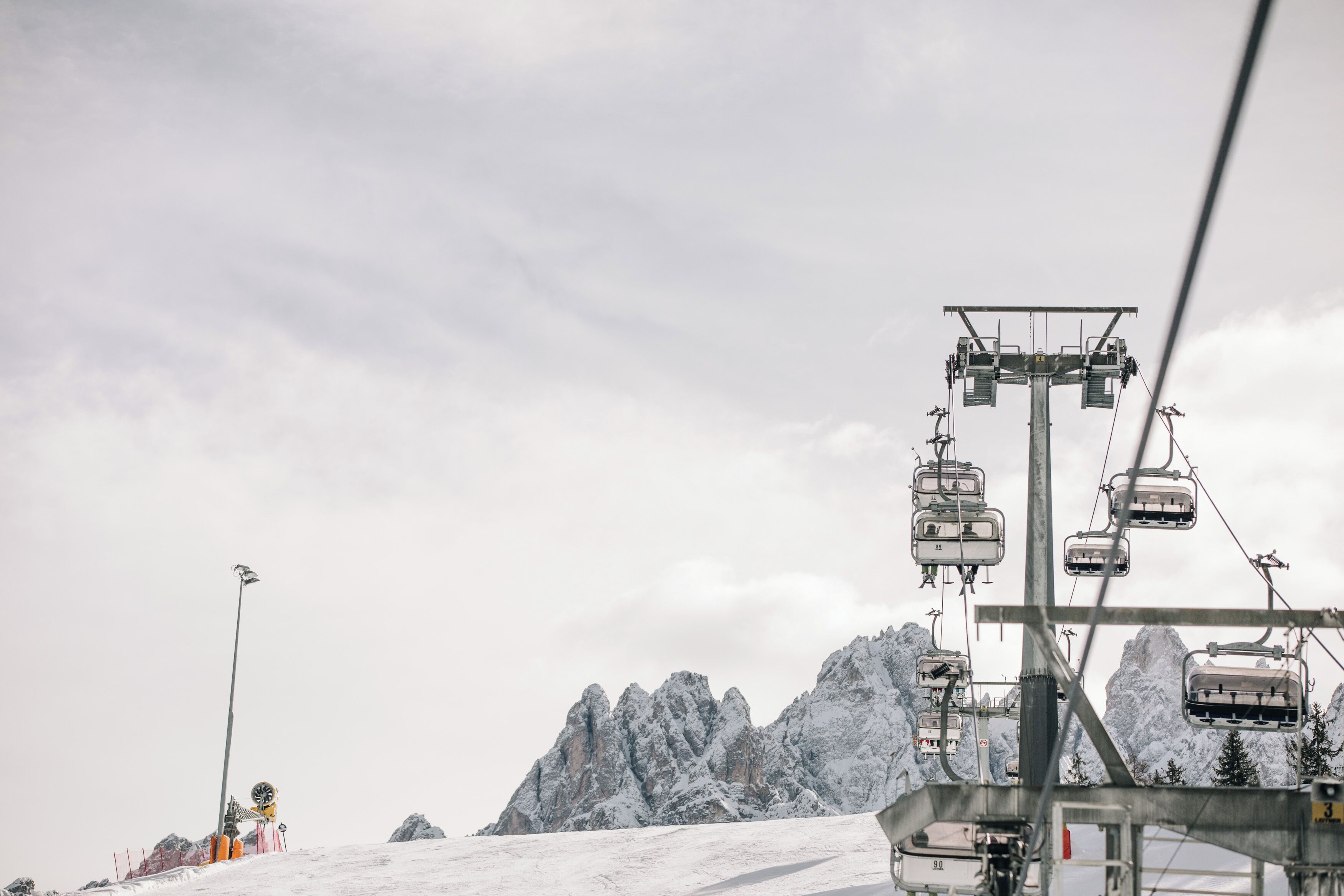 Un telesilla con cables y asientos frente a un paisaje montañoso nevado.