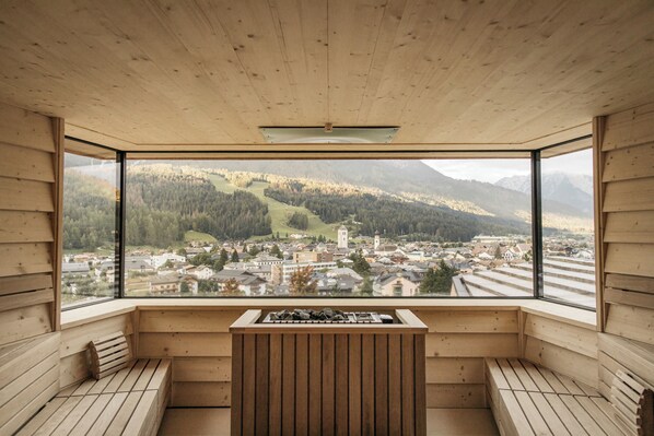 Interior de madera con un amplio ventanal que ofrece vistas a un pueblo y montañas.