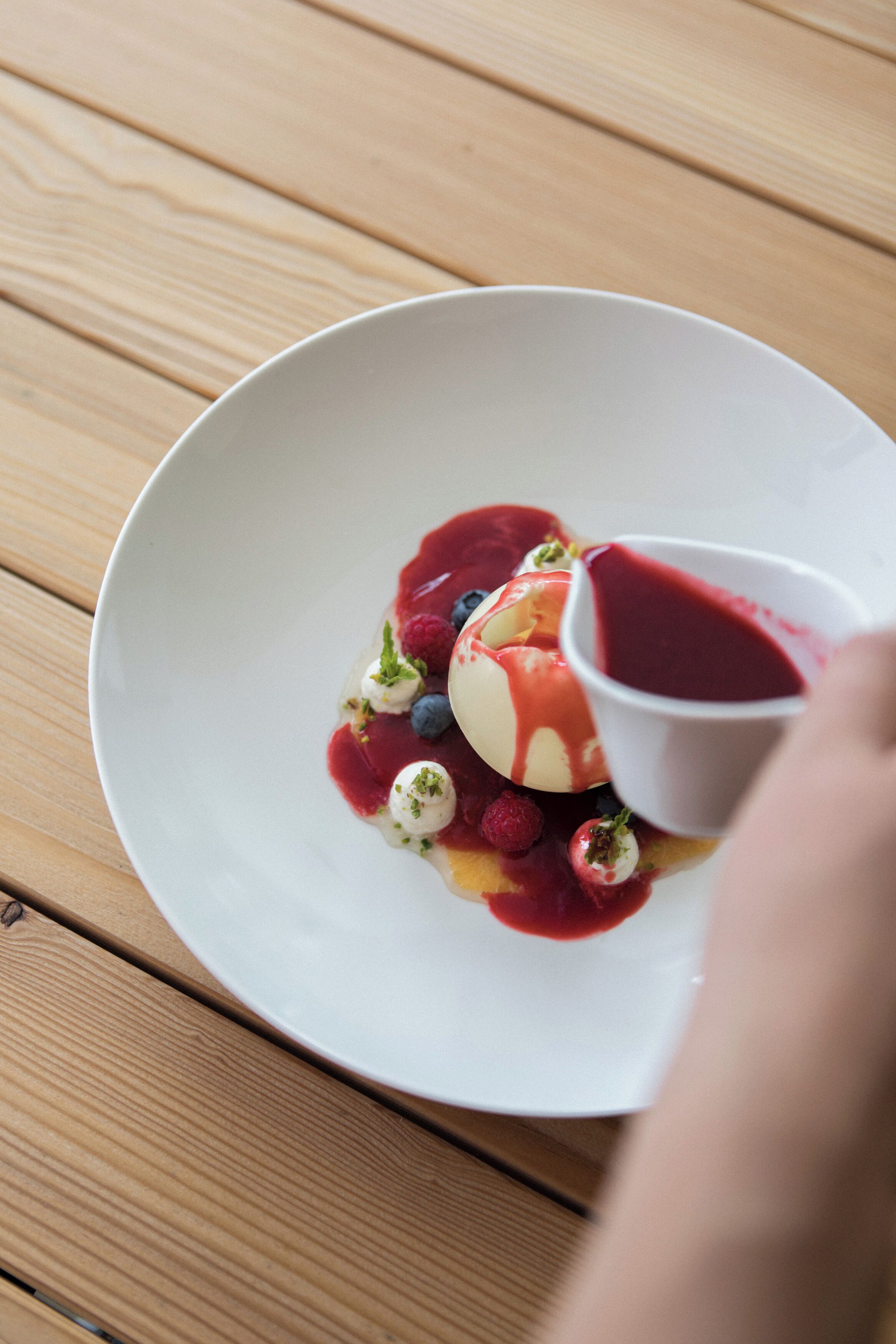 Dessert auf einem weißen Teller mit Beeren und einer kleinen Schale Soße.