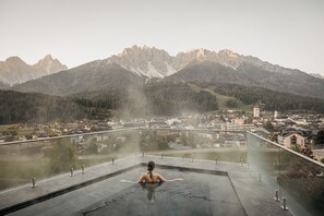 Una persona en una bañera de hidromasaje con vistas a un pueblo y montañas al fondo.