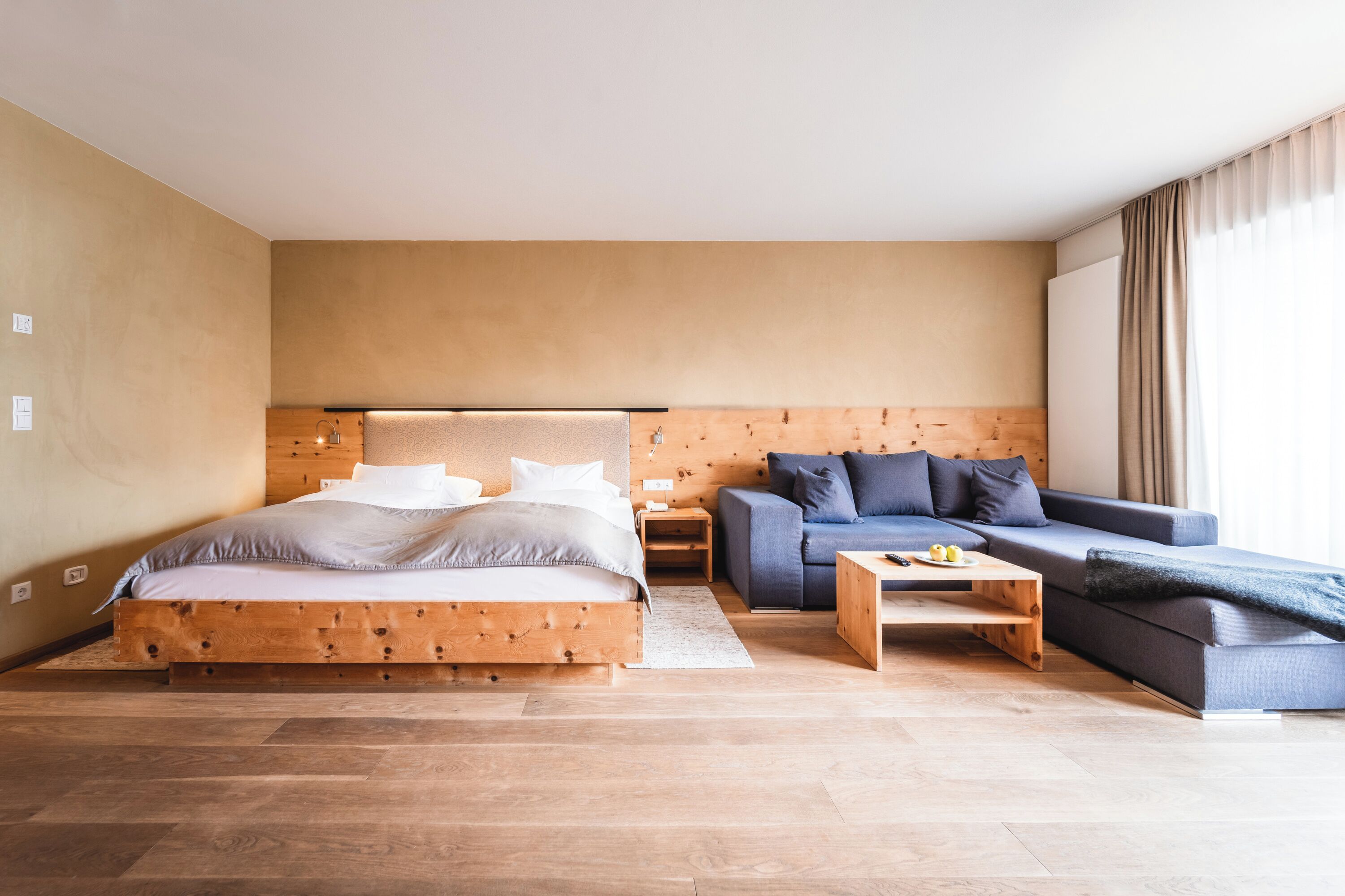 A modern bedroom with a wooden bed, a blue sofa, and a wooden coffee table.