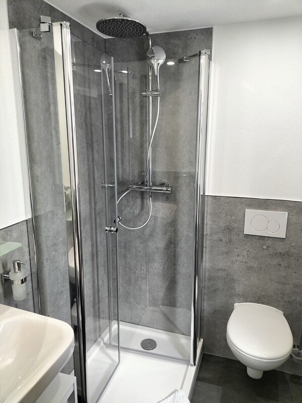 Un baño moderno con ducha envuelta en vidrio, inodoro blanco y lavamanos con dispensador de jabón.