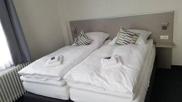 Un lit simple avec une literie et des oreillers blancs, une table de chevet avec une lampe et un radiateur.