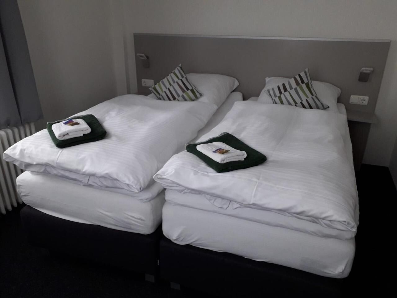 Two single beds with white linens and striped pillows, a grey headboard, and a bedside table with a lamp.
