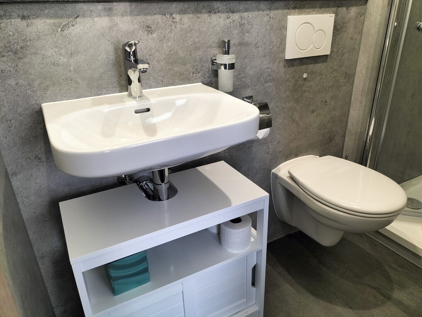Een badkamer met een witte wastafel, toilet en douche.