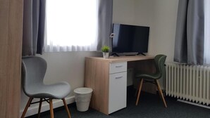 Una habitación pequeña y moderna con un escritorio, dos sillas, un televisor y un radiador.