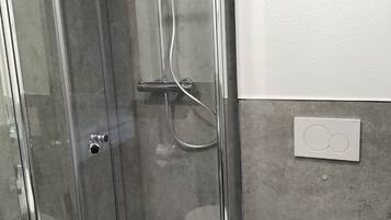 A modern bathroom with a glass-enclosed shower, a white toilet, and a small sink.