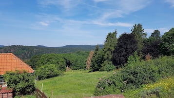 A rural landscape with a house featuring a red-tiled roof, surrounded by lush greenery and trees.