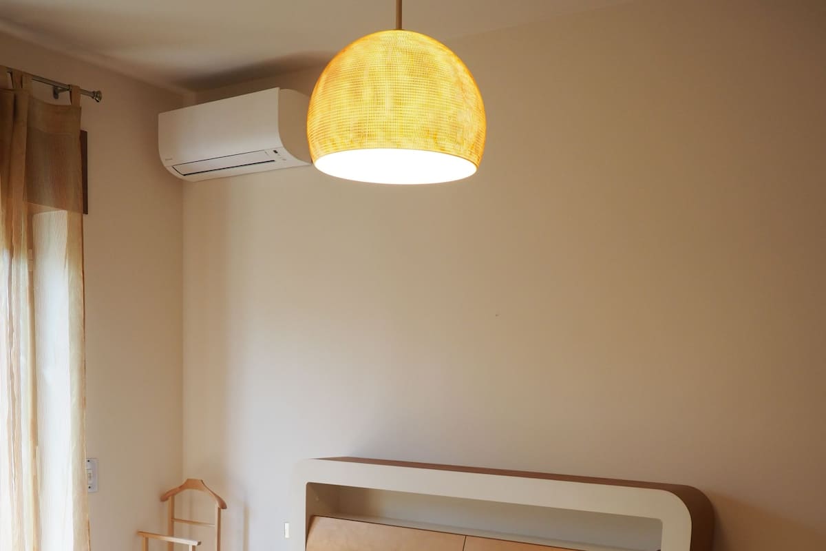 A bedroom with a bed, a nightstand, a hanging lamp, and an air conditioning unit.