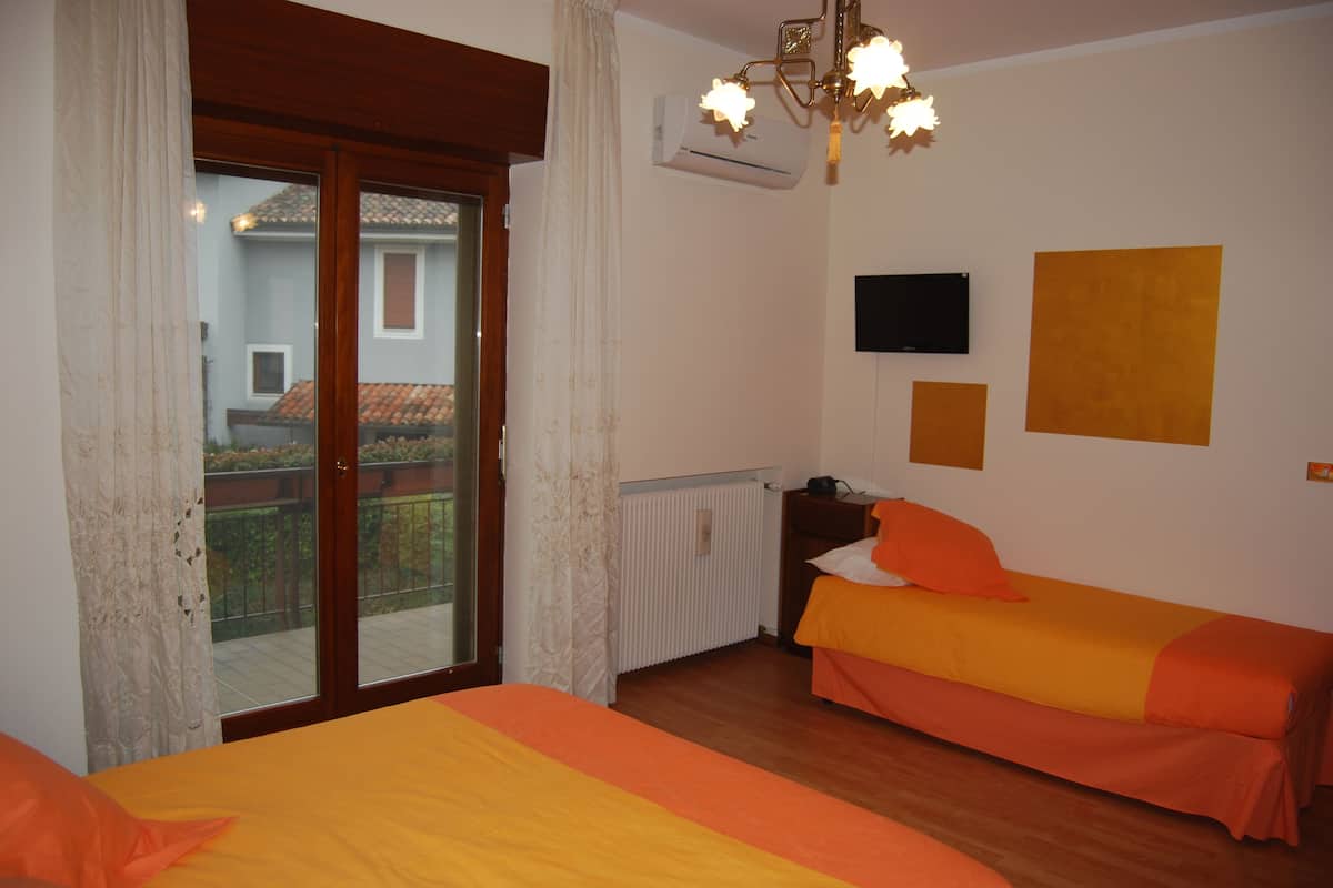 A bedroom with two beds, a sliding glass door to a balcony, an air conditioning unit, and a mounted TV.