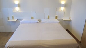 A neatly made bed with white linens and a beige skirt. There are two bedside tables with lamps on either side of the bed. - Bed & Breakfast Villa Filotea (Desenzano del Garda)
