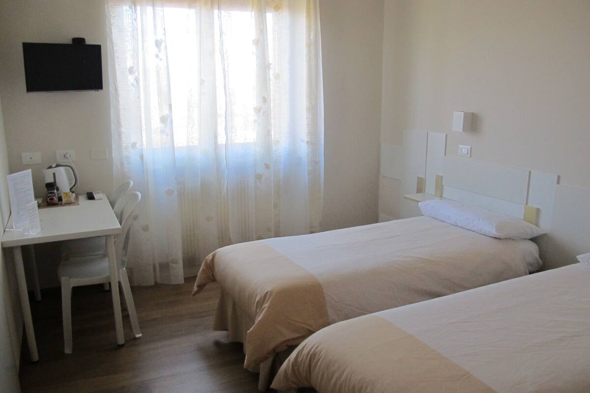 A hotel room with two beds, a desk, a chair, and a TV mounted on the wall.