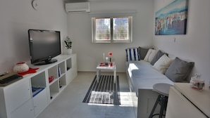 Una sala de estar moderna con una televisión de pantalla plana, un sofá, una mesita con una planta y un cuadro en la pared.