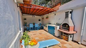 Un patio al aire libre con una mesa azul, sillas, una parrilla y plantas en macetas.