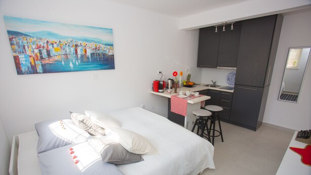 Una habitación de hotel moderna con cama, un cuadro, kitchenette y un pequeño comedor.