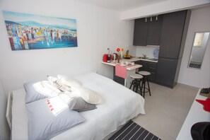 A modern hotel room with a bed, a painting, a kitchenette, and a small dining area. - Studio Apartment Laganini (Split)