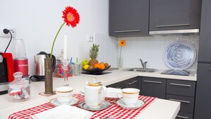 Una cocina con una mesa de comedor dispuesta para dos personas, con mantel a cuadros rojo y blanco, platos blancos, tazas con detalles dorados y un florero con una flor roja.