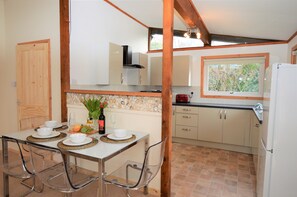Una cocina con comedor, que incluye una mesa blanca con sillas transparentes, un salpicadero de piedra y vigas de madera.