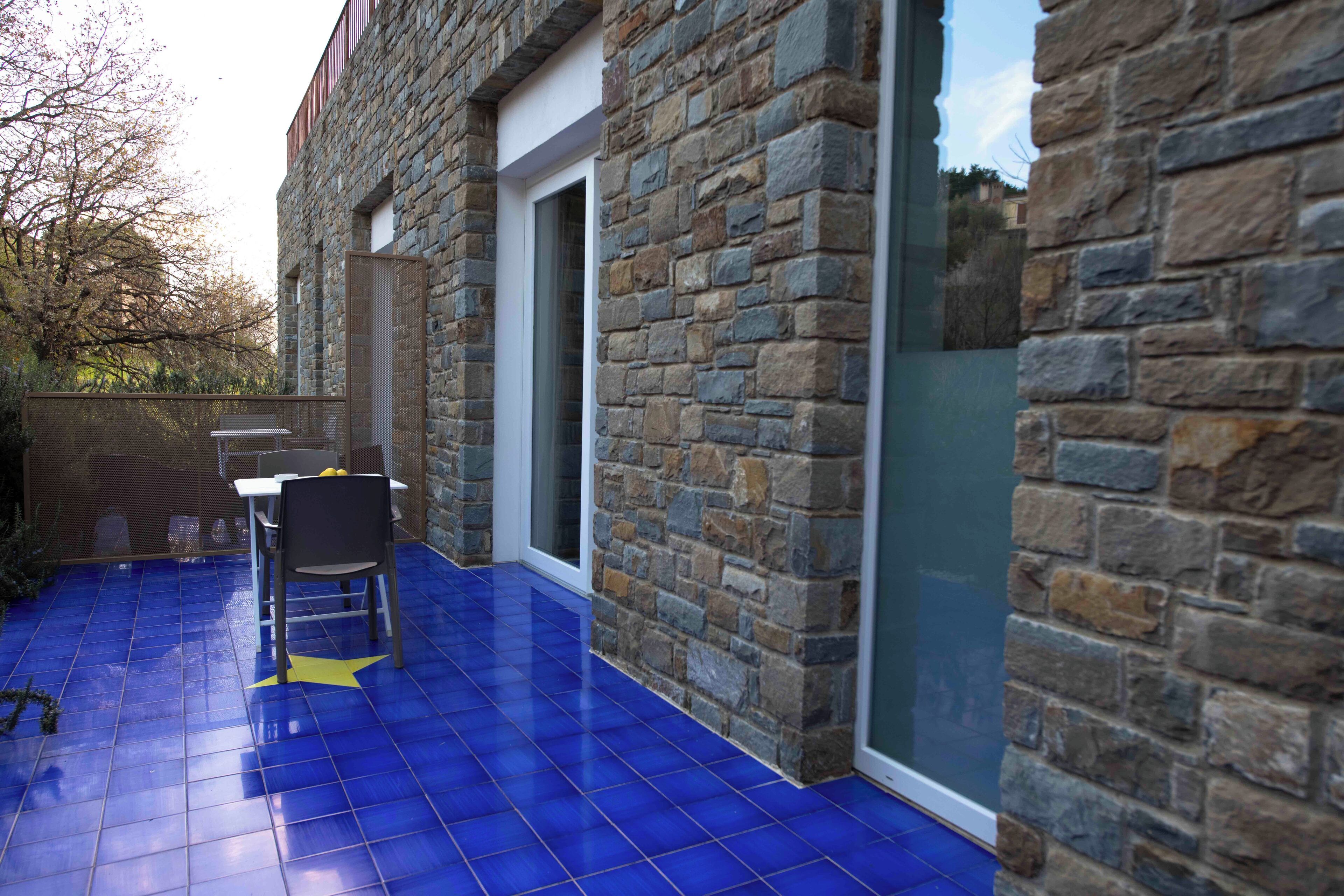 A stone building with a blue-tiled patio, a chair, and a table.