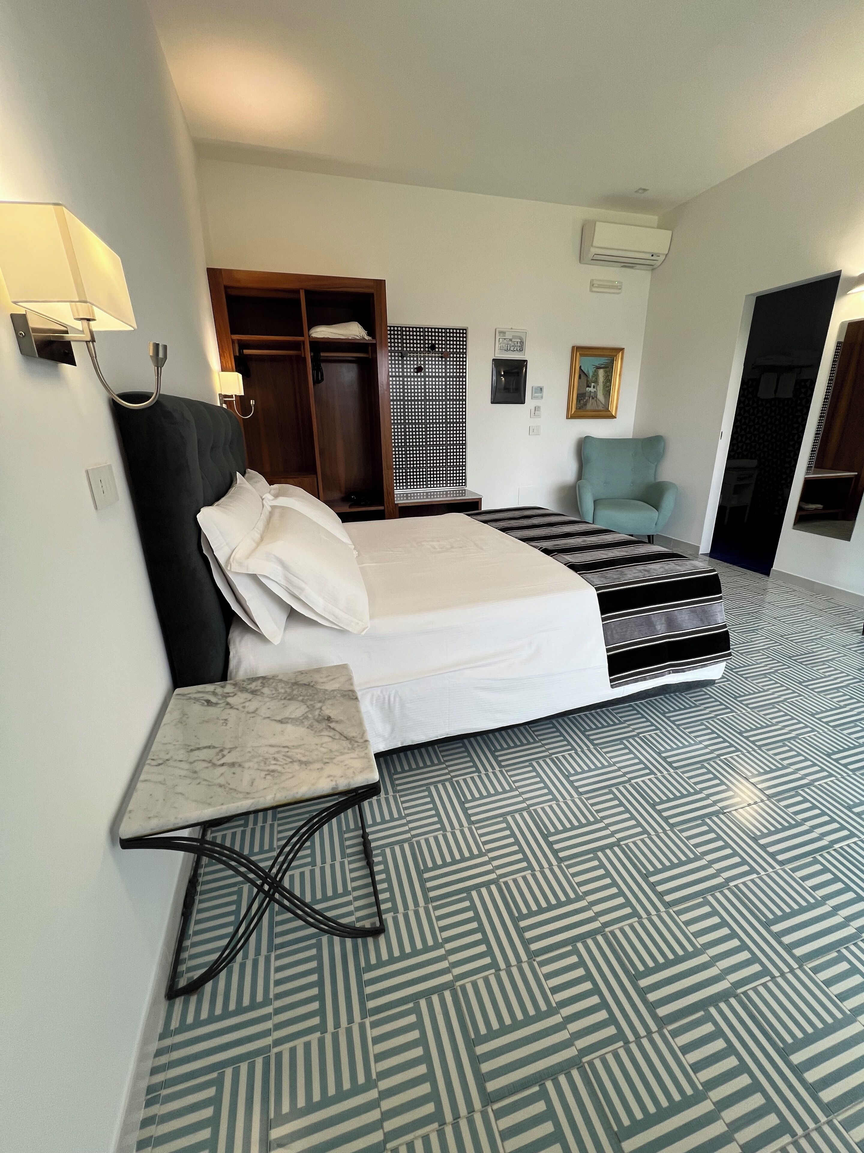 Une chambre d’hôtel comprenant un lit, une petite table, une chaise, une armoire et un panneau décoratif mural.