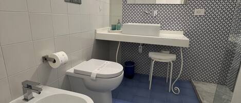 A bathroom with a white sink, a toilet, and a bidet. There is a mirror above the sink and a patterned wall behind it.