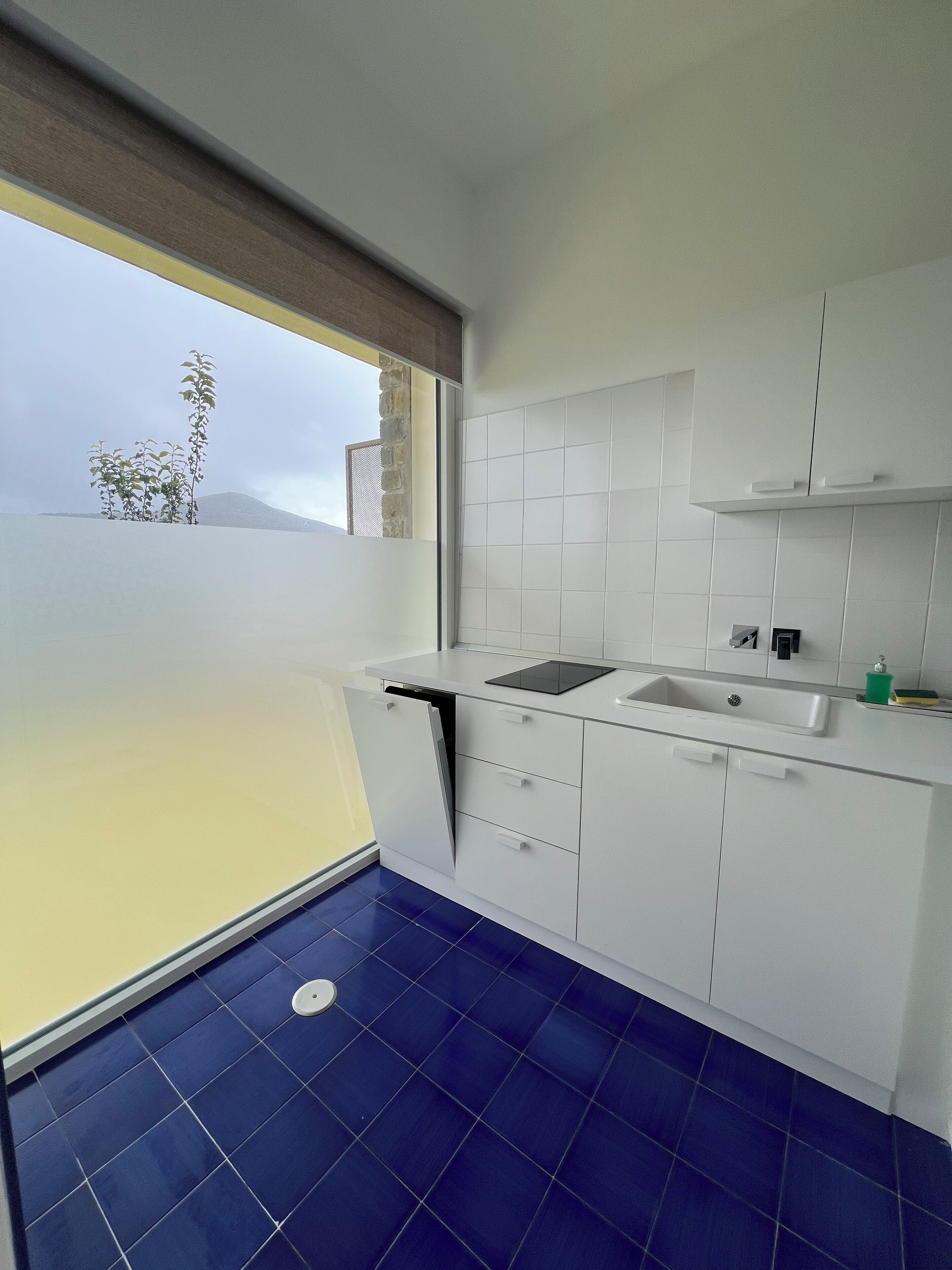 Una cucina moderna con mobili bianchi, un lavello e una finestra con vista su un balcone.