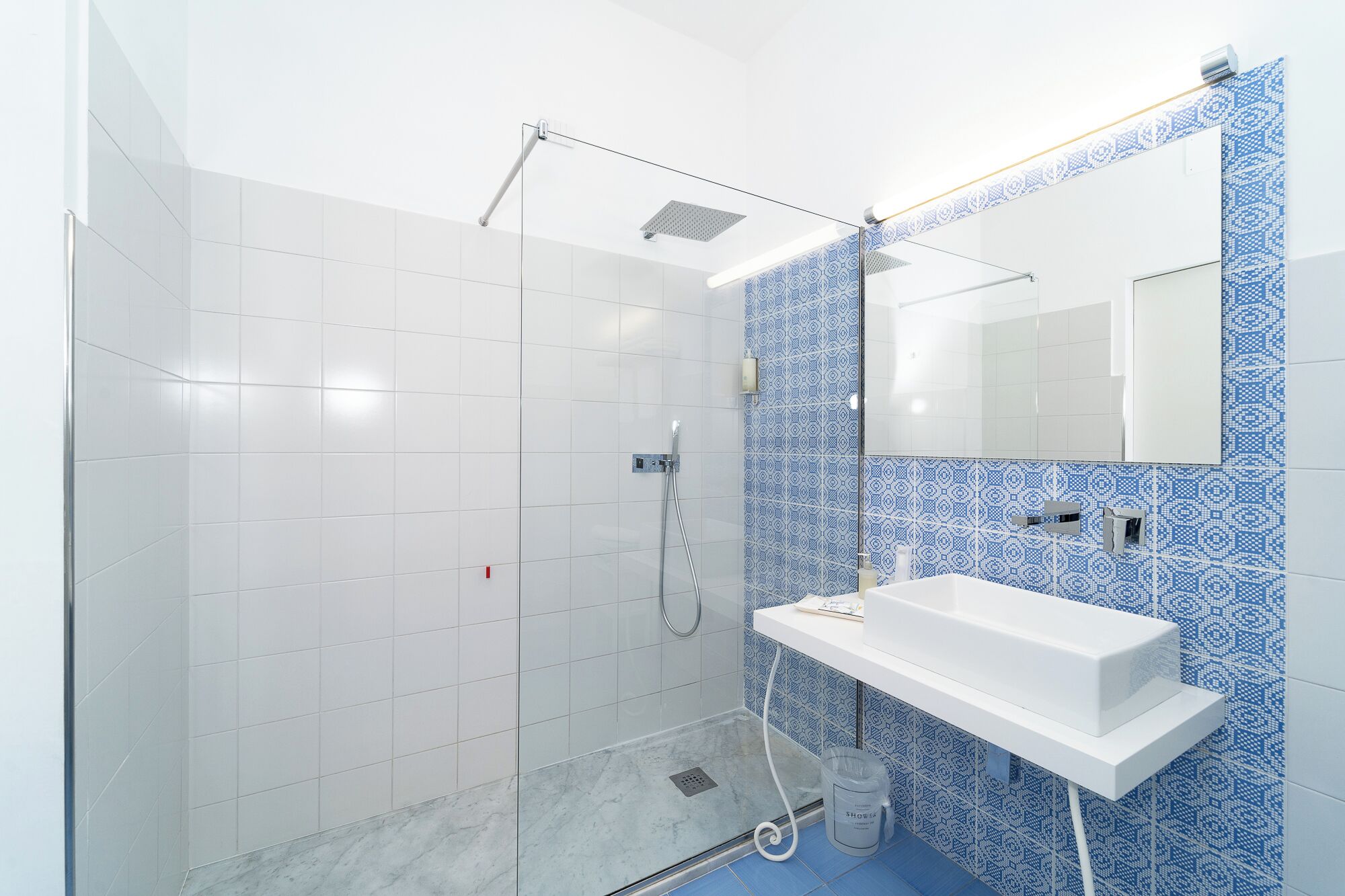 A modern bathroom with a shower, a white sink, and a patterned wall.