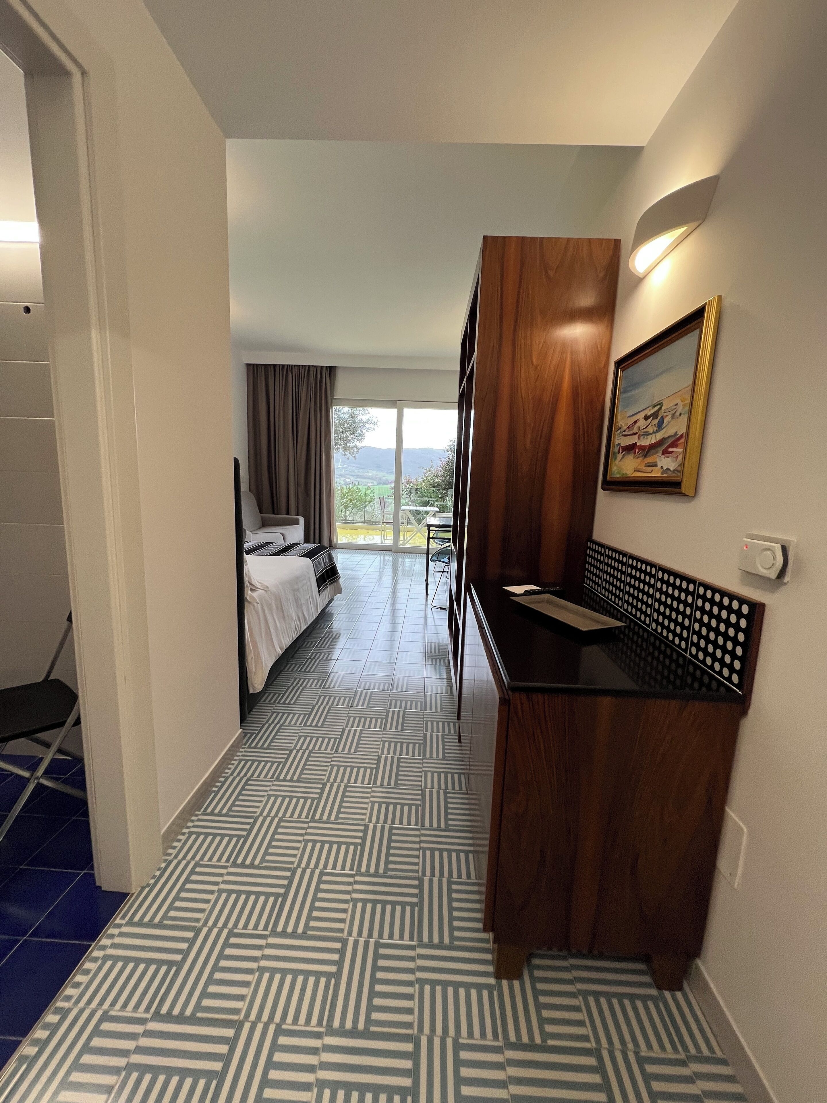 Una camera d'albergo con un letto, una scrivania, una sedia, un quadro appeso e vista all'esterno.