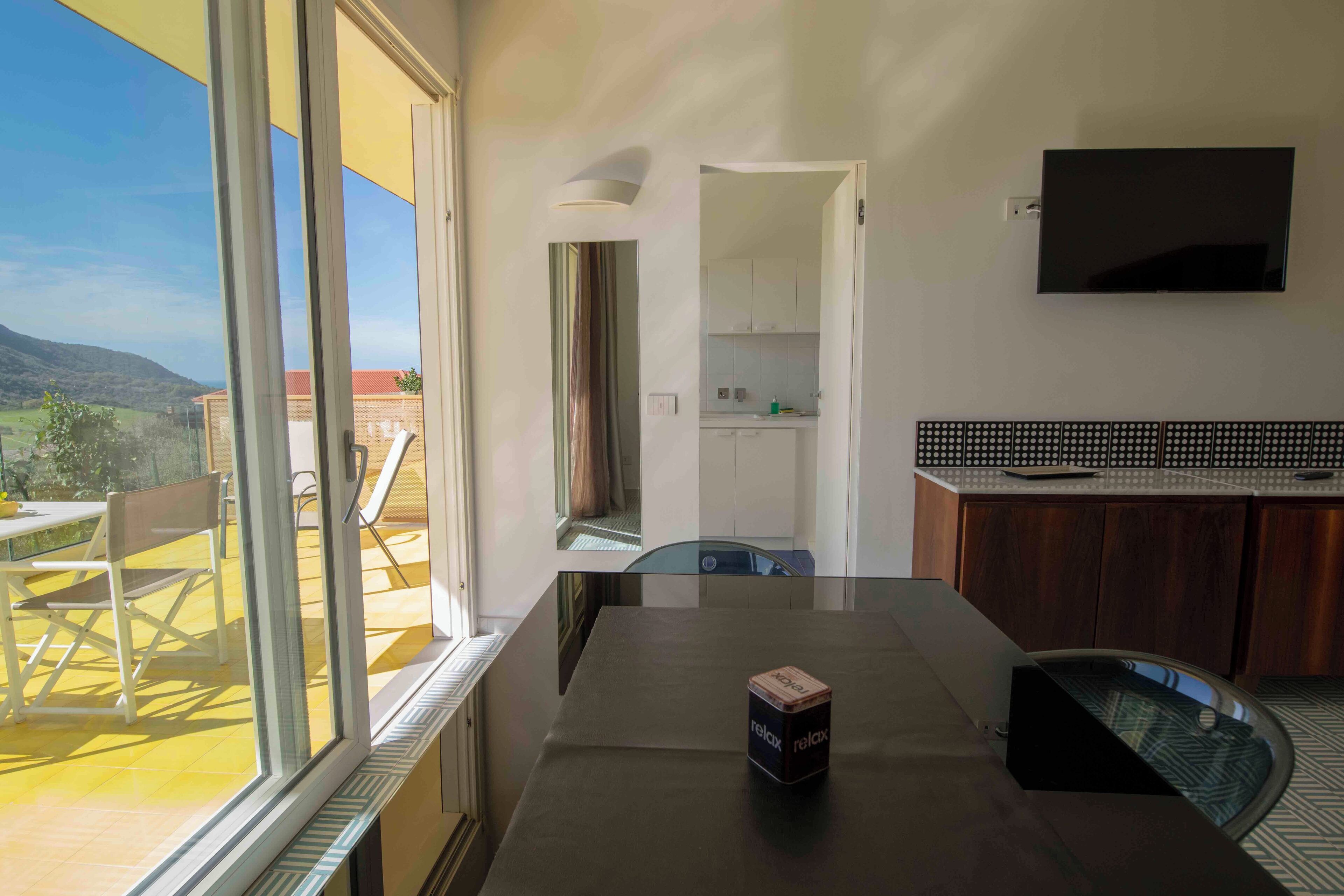 A modern kitchen with a large window, a dining area with a table and chairs, and a TV mounted on the wall.