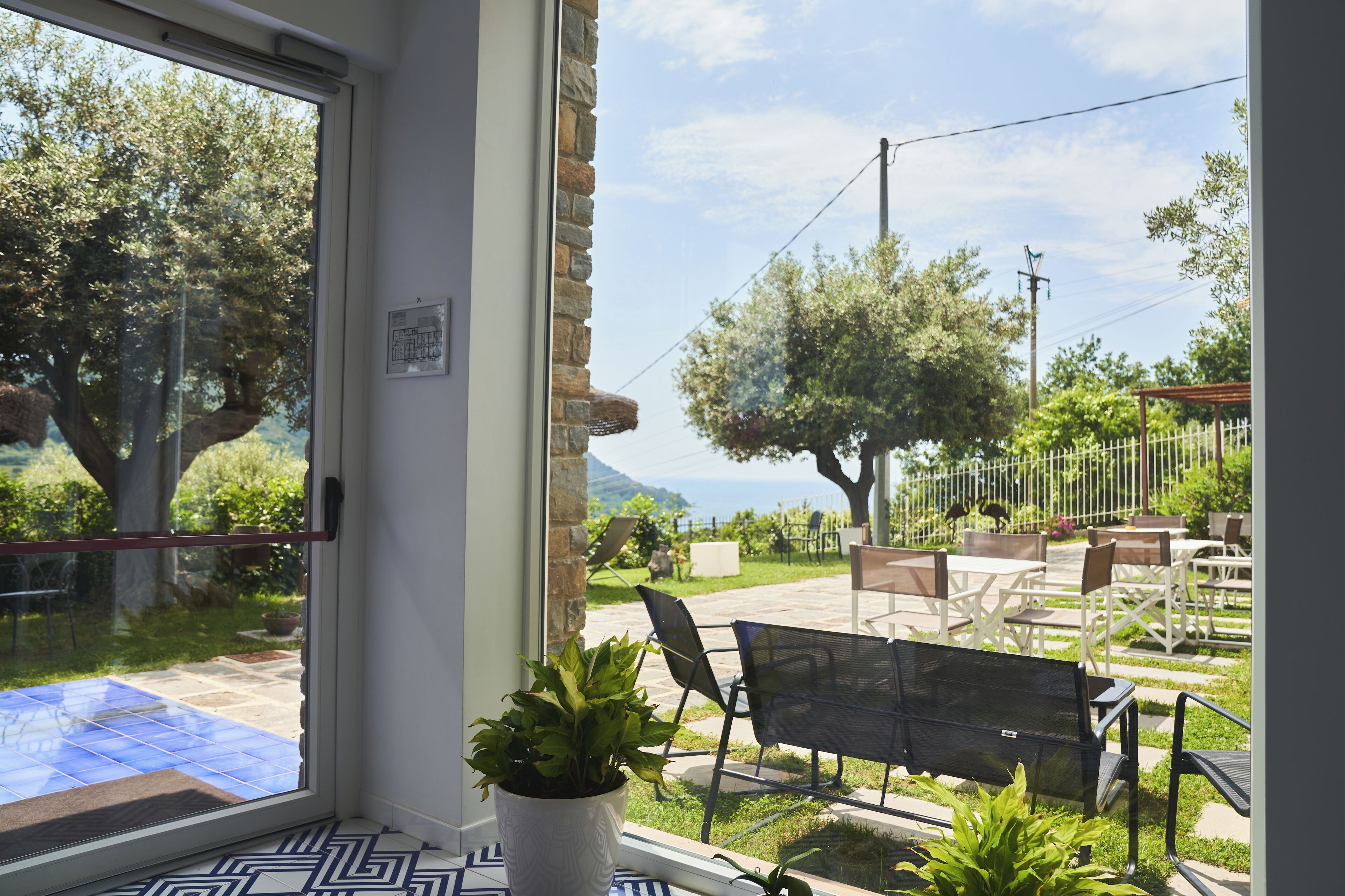A patio area with a bench, potted plants, and a view of the outdoors including trees and a fence.