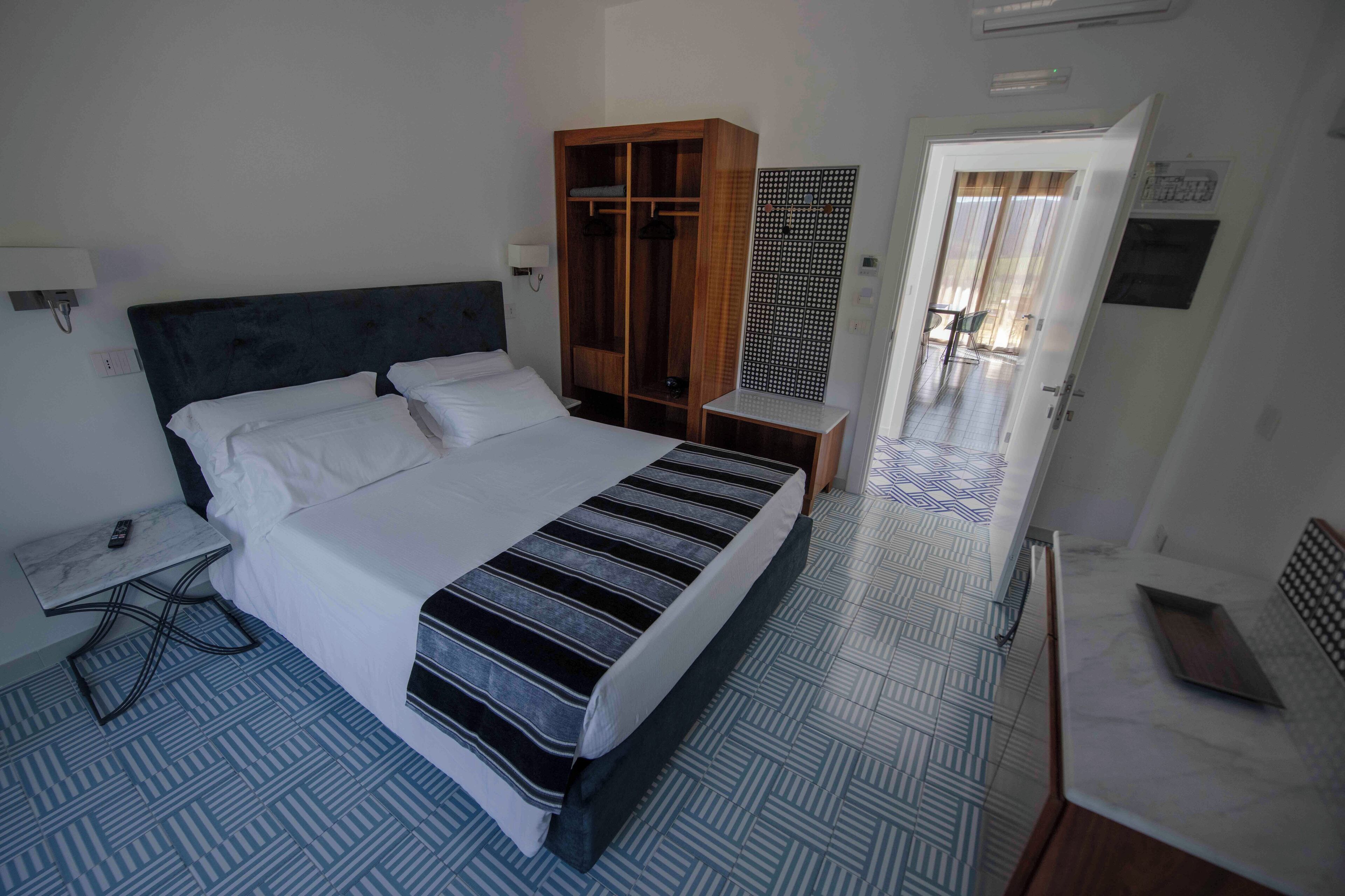 Una habitación de hotel con una cama grande, un armario, una mesita de noche y un escritorio pequeño con una silla.