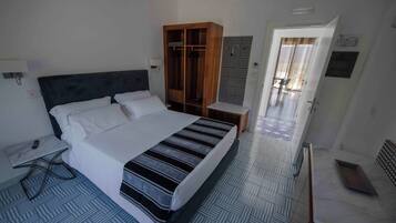 Una habitación de hotel con una cama grande, un armario, una mesita de noche y un escritorio pequeño con una silla.