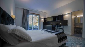 Une chambre d’hôtel moderne dotée d’un grand lit, d’une kitchenette et d’une porte-fenêtre coulissante donnant sur l’extérieur.