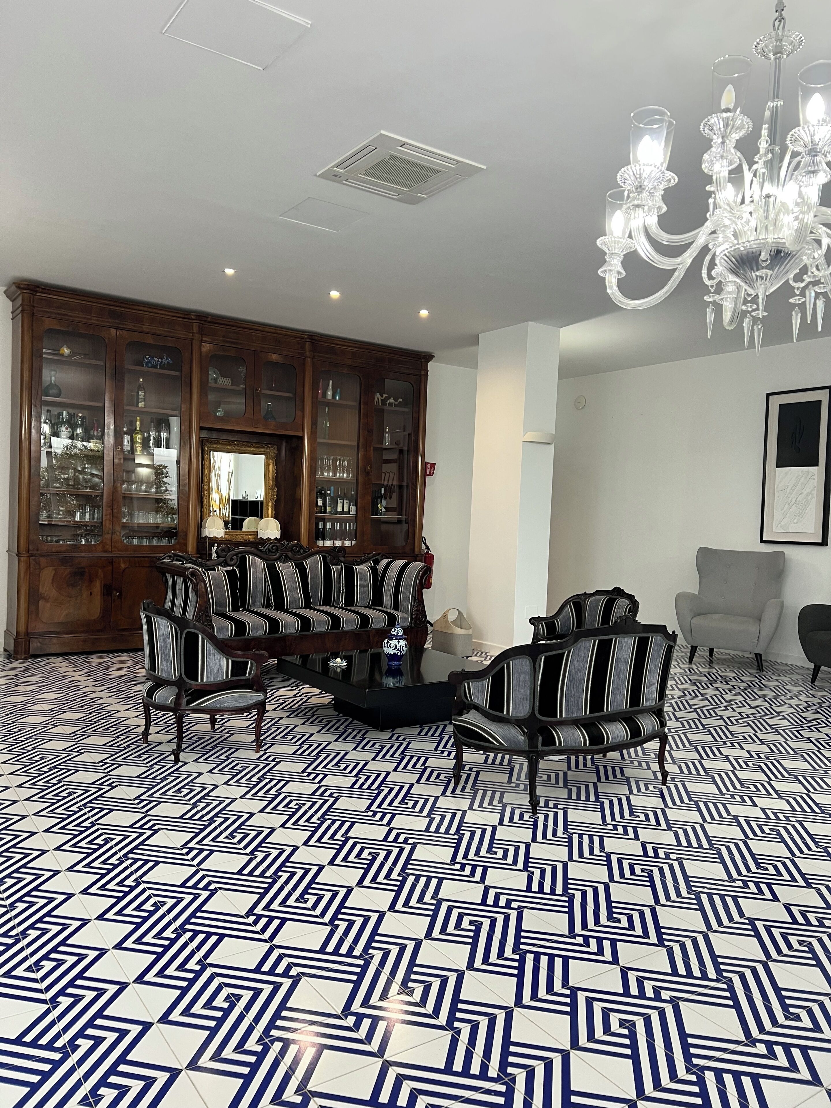 A room with a geometric patterned floor, a mirrored cabinet, striped upholstered chairs, and a chandelier.