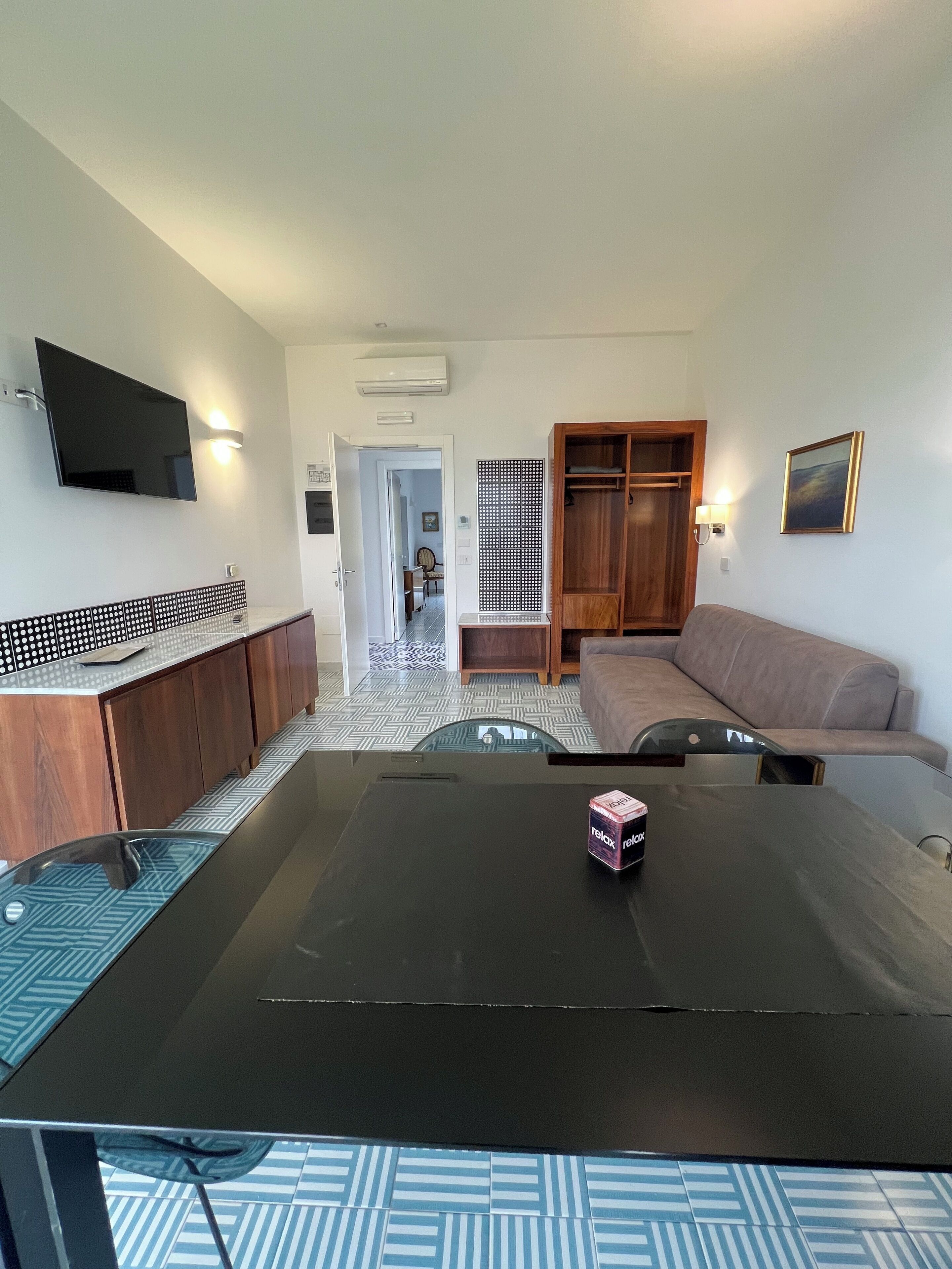 A modern living room with a black coffee table, a beige sofa, a wooden cabinet, and a TV mounted on the wall.