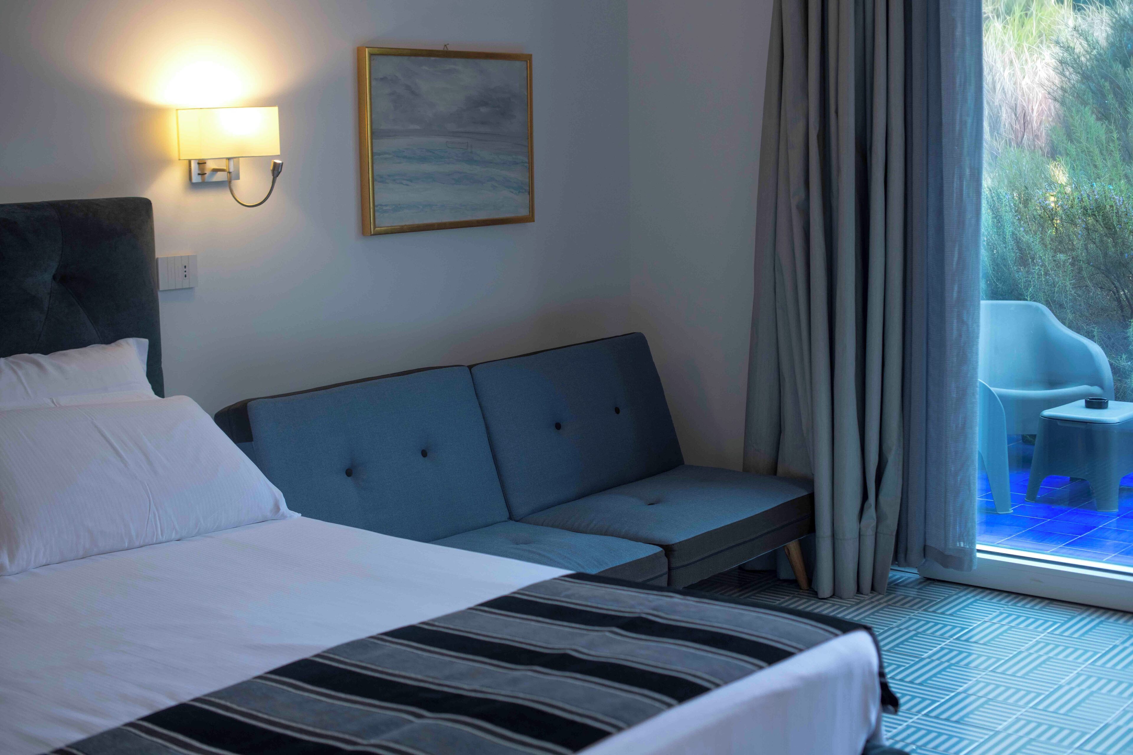 Une chambre d’hôtel avec un lit, un canapé, une lampe fixée au mur et un tableau.