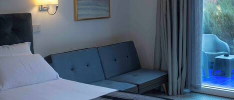 Une chambre d’hôtel avec un lit, un canapé, une lampe fixée au mur et un tableau.