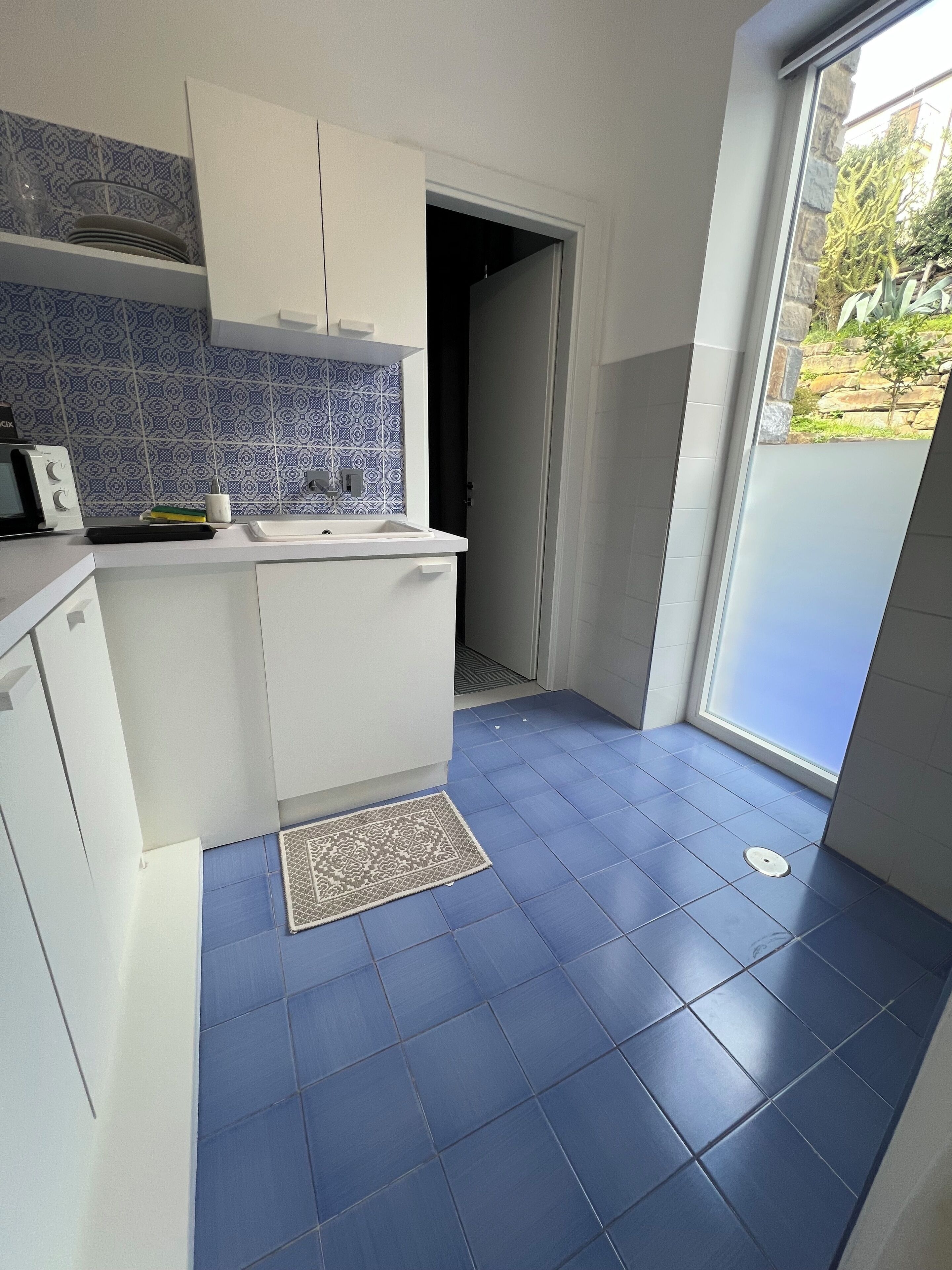 Una cocina pequeña con gabinetes blancos, un salpicadero de azulejos azules y un suelo también de azulejos azules.