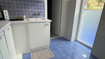 Una cocina pequeña con gabinetes blancos, un salpicadero de azulejos azules y un suelo también de azulejos azules.