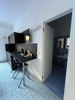 Cocina moderna con encimera negra, horno empotrado y microondas. Hay una ventana sobre la encimera y una puerta que da a un baño.