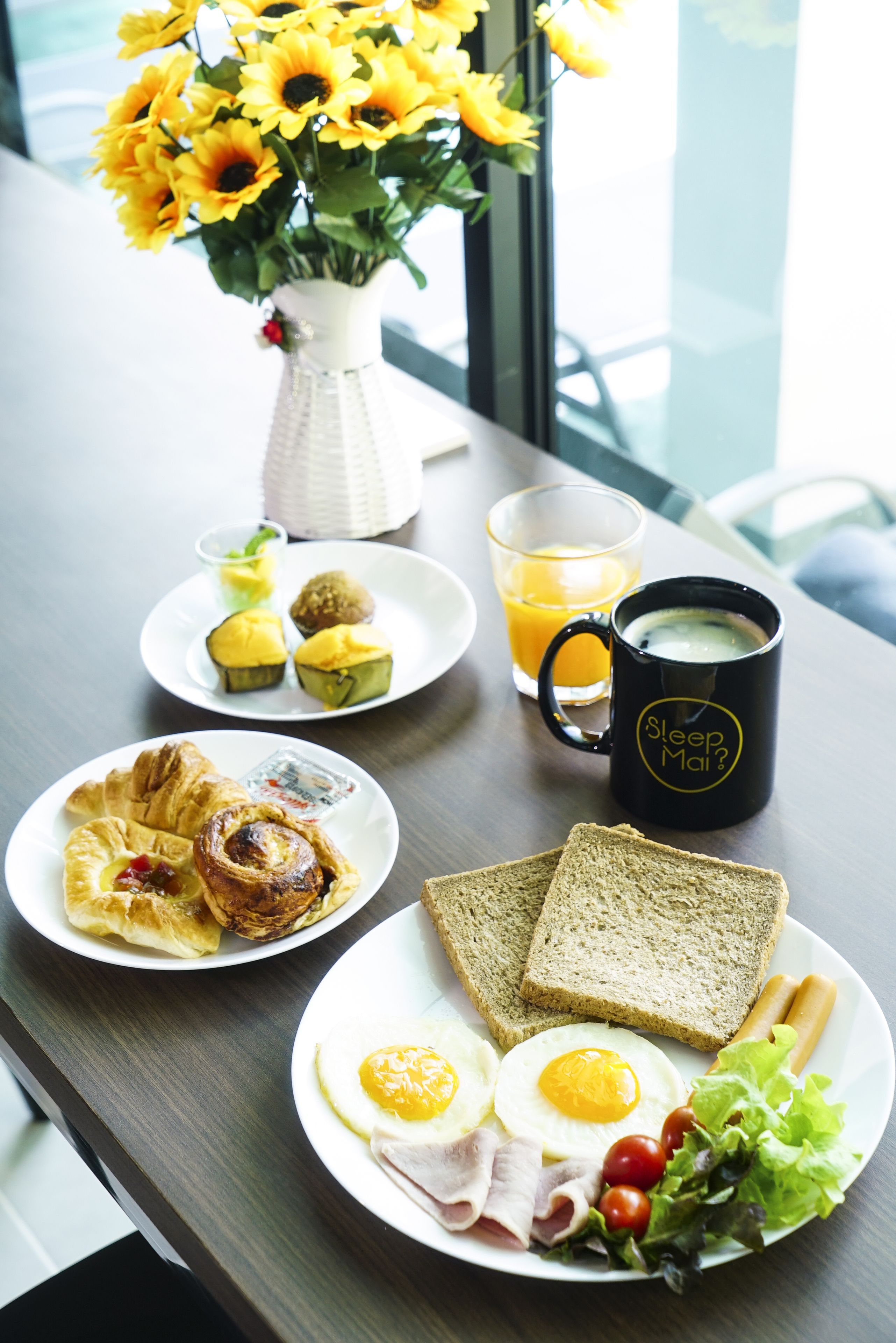 Una mesa de desayuno con platos de comida, una taza de café y un jarrón de flores.