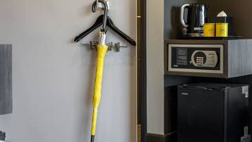 Habitación de hotel con minibar negro, cafetera y un paraguas amarillo colgando de un perchero de pared.