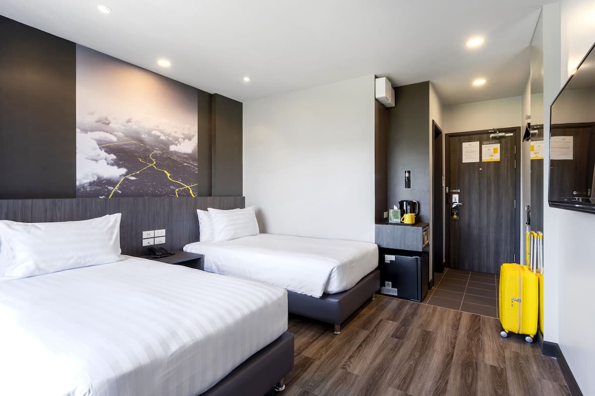 A hotel room with two beds, a small desk, a mirror, and a wall-mounted artwork.